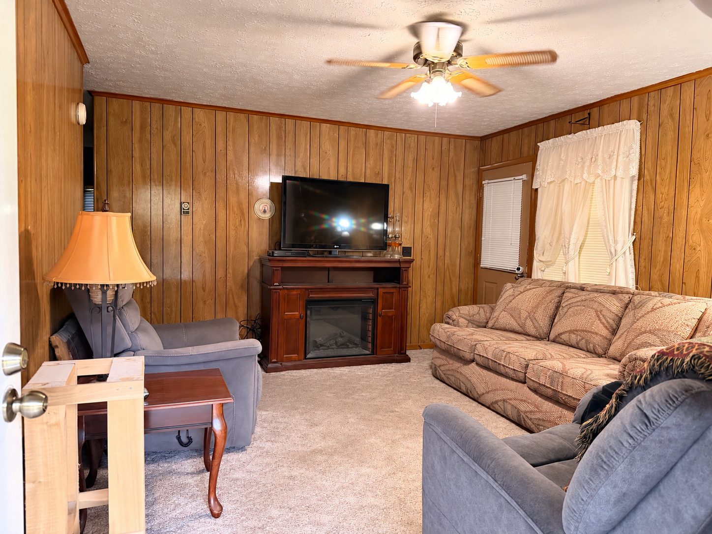 Wood-paneled living room with ceiling fan and carpet